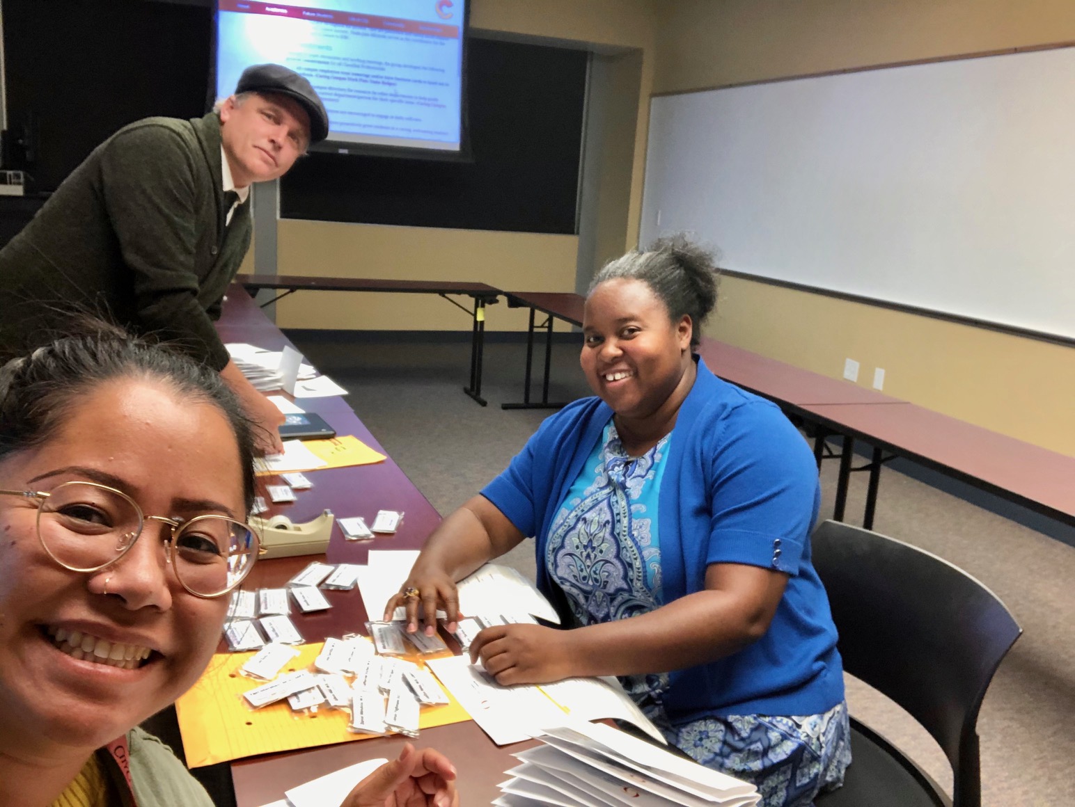 Photo of Classified Senate President Awana Payne, Vice President Sean Ryan, and Professional Development Coordinator Paula Miranda sorting name badges for delivery