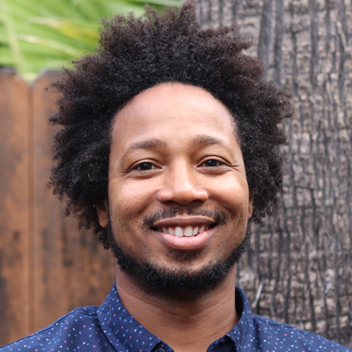 headshot of smiling black male wearing a blue button up shirt with pattern